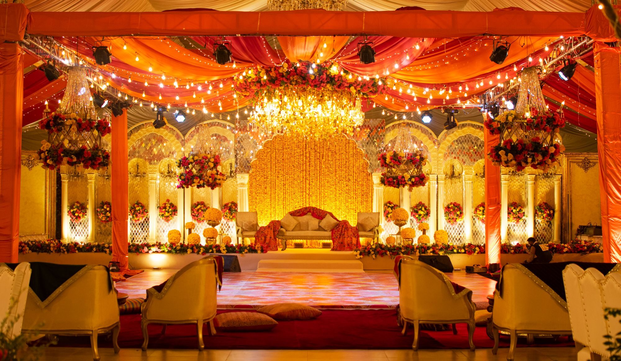 A mandap hall under amber drapes, chandeliers and floral pillars