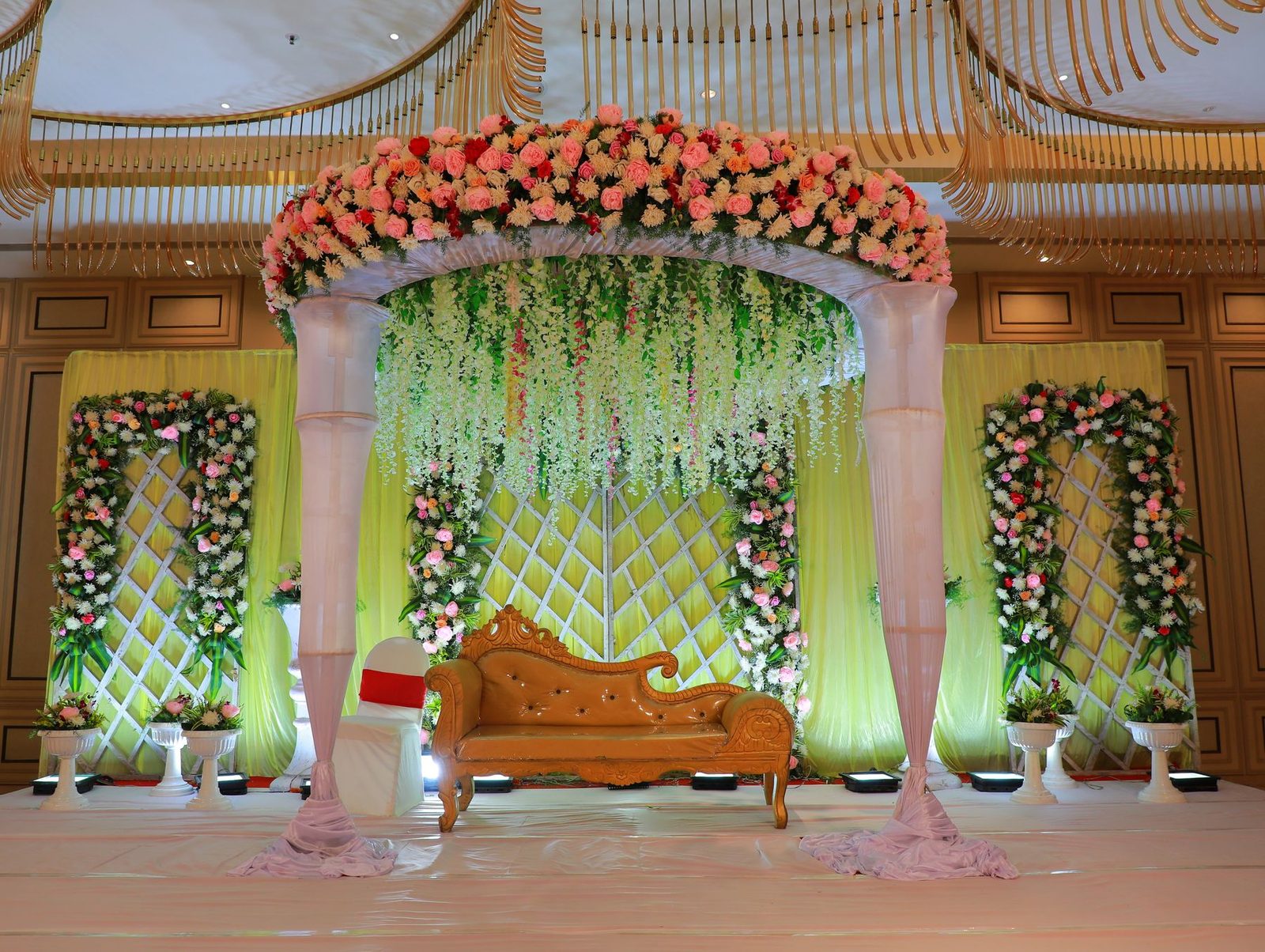 A floral mandap with decorated pillars and a carved seat